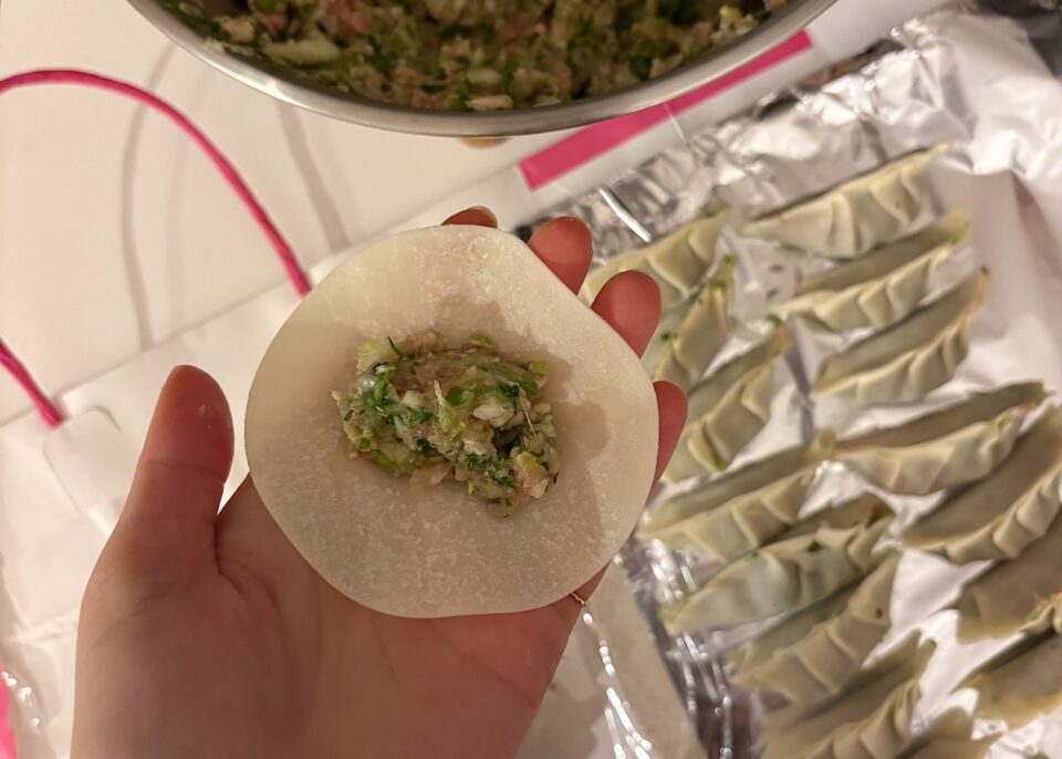 餡を乗せた餃子を手のひらに乗せている