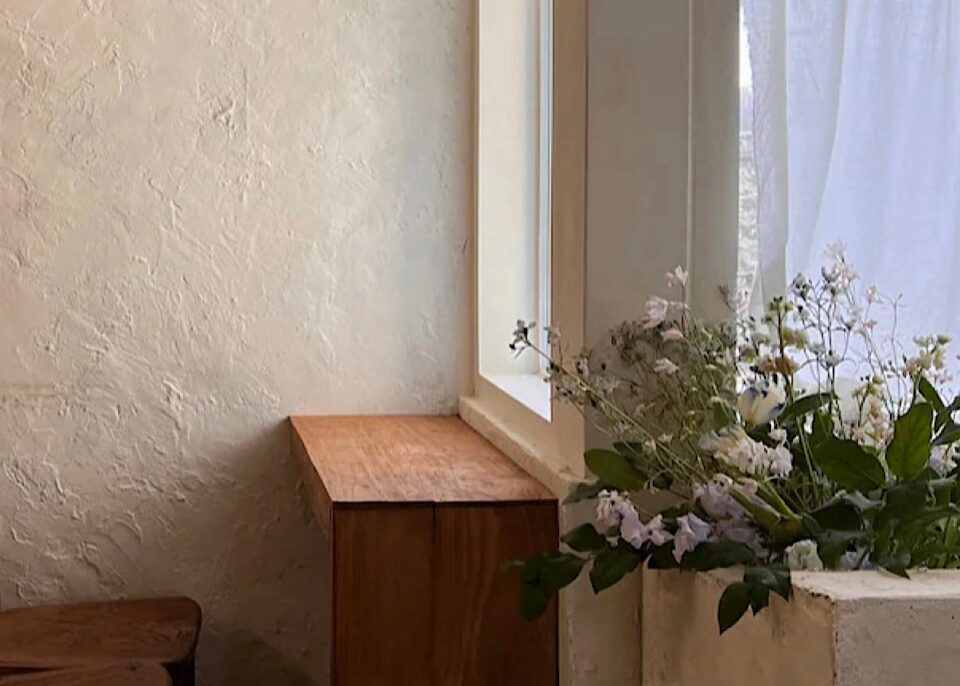アイボリーの壁紙の部屋に、ブラウンのウッドテーブル、小さなお花が飾られている